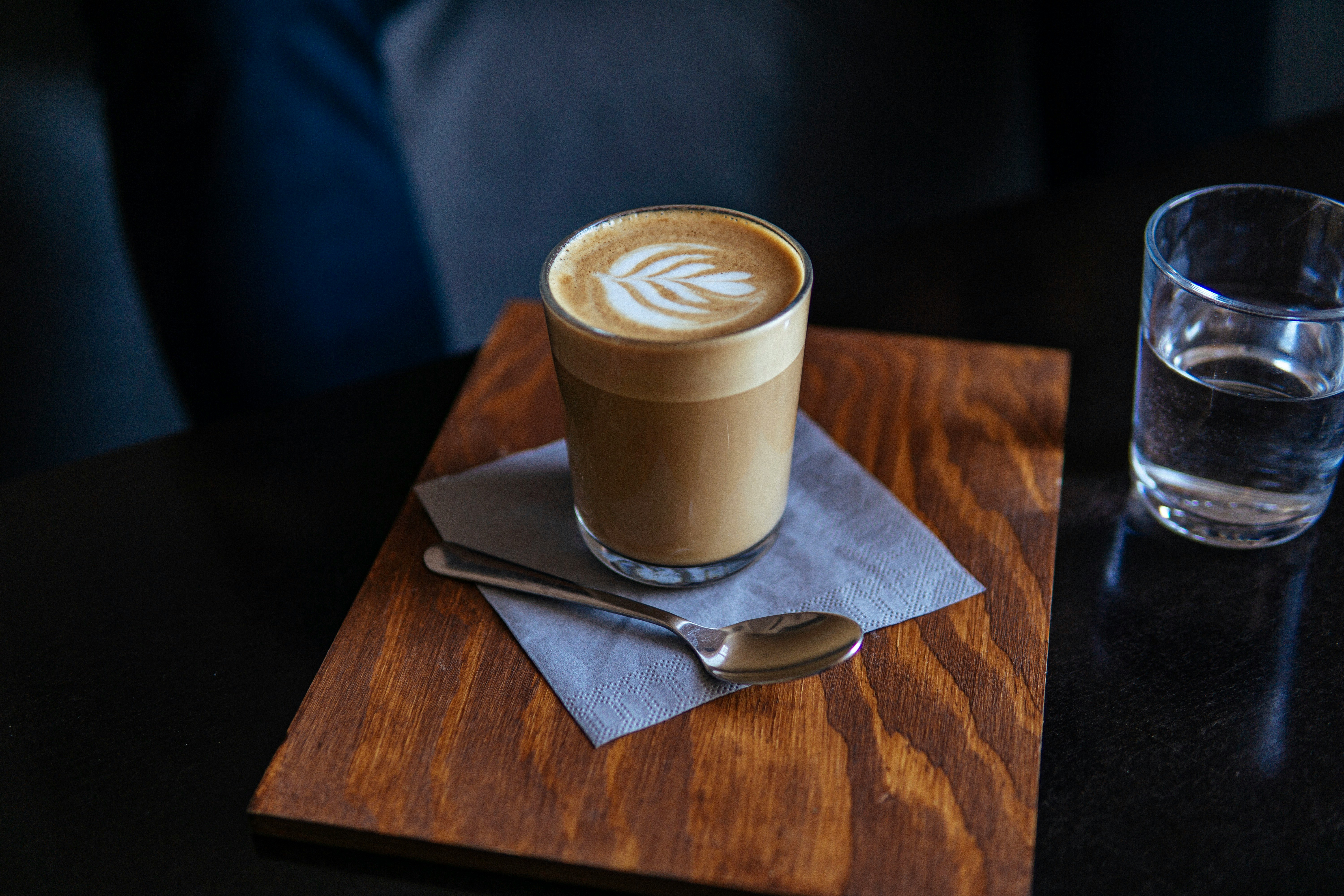 cappuccino in drinking glass near gray stainless steel spoon